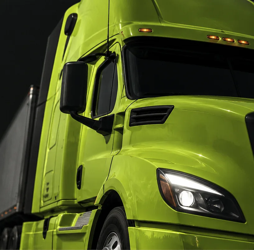 The nose of a lime-green tractor and its trailer, lit against black.
