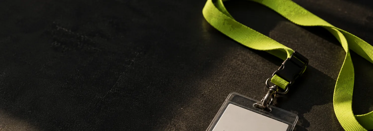 A lime-green DEM lanyard left on a dark worn desk in late afternoon light, its badge running off the bottom of the frame.